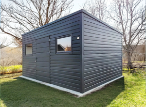 4,8x3,3m-es delux fém kerti tároló hátra lejtő tetővel, antracitszürke színben, ajtóval, 2db ablakkal, ereszcsatornával, szegélyekkel, horganyzott vázszerkezettel, vízszintes lemezborítással