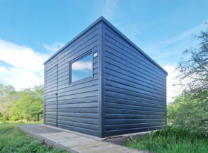 3x3m-es delux fém kerti tároló hátra lejtő tetővel, fahatású szürke színben, ajtóval, ablakkal, ereszcsatornával, szegélyekkel, horganyzott vázszerkezettel, vízszintes lemezborítással